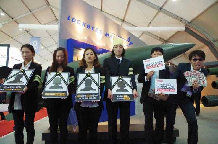 Activists stand in front of the Lockheed Martin exhibit at the ADEX arms fair