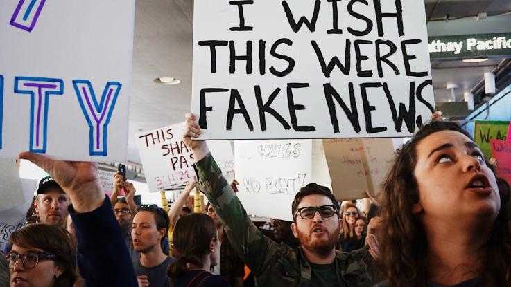 A protester holds a placard reading "I wish this were fake news"