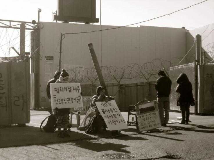 A handful of activists sit in front of the gates of the naval base being built on Jeju Island