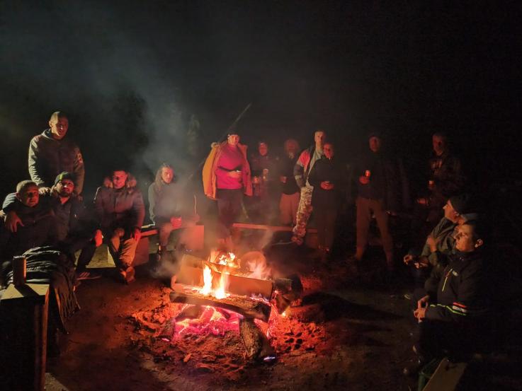 The photo is taken at night. A number of people are sitting around a fire.