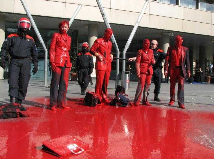 Activists covered in red paint outside a bank that funds the arms industry
