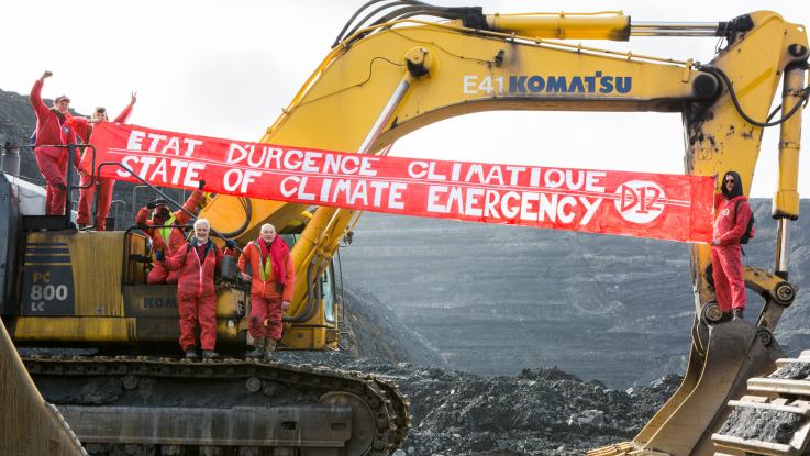 Climate activists occupy a digger in a coal mine, and hang a large red banner reading "Climate emergency!"