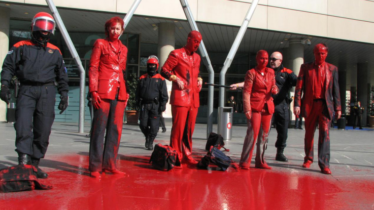 Activists stand in front of a bank, covered in red paint, in a protest against funding of the arms trade.