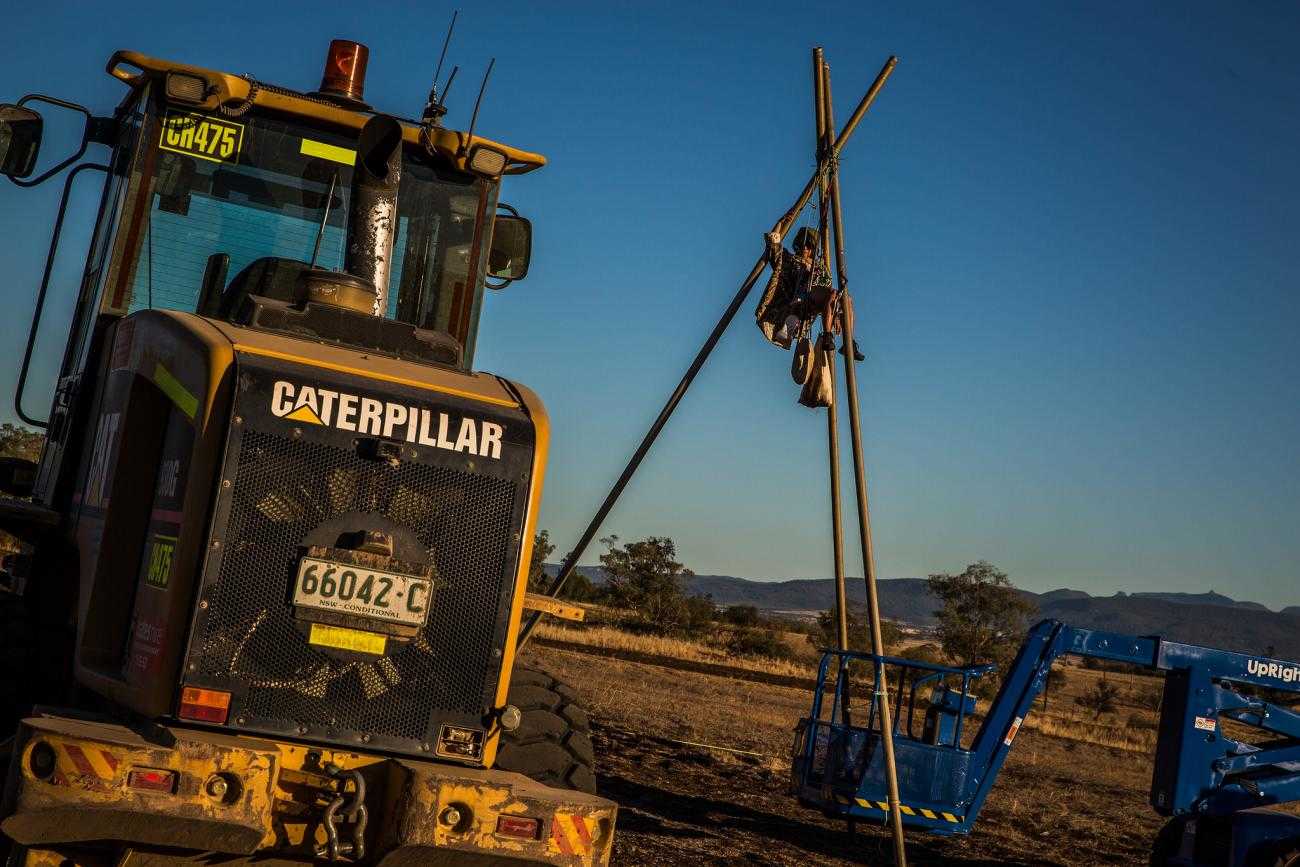 An activist has climbed a tripod made out of metal poles to stop a construction vehicle at a coal mine