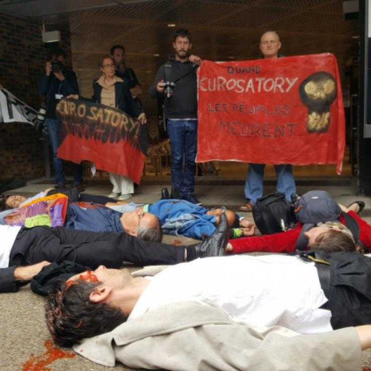A large group of people lie on the floor in front of banners outside the Eurosatory arms fair