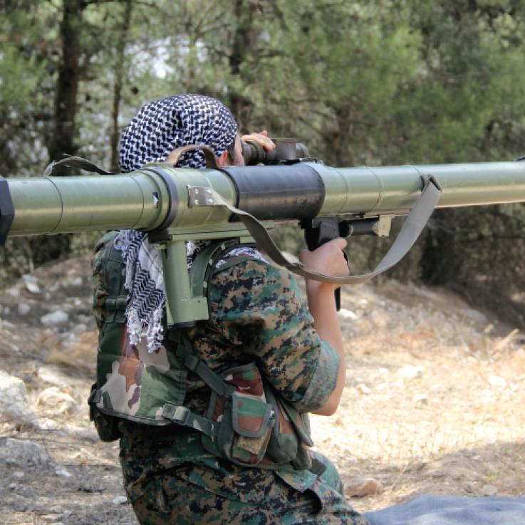 A man with his back tot he camera holds a large rocket launcher over his shoulder