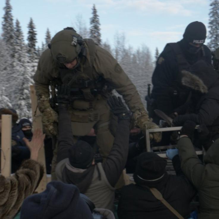 Varios policías con uniforme de combate suben a una barrera. En el patio un gran número de activistas intentan detenerlos